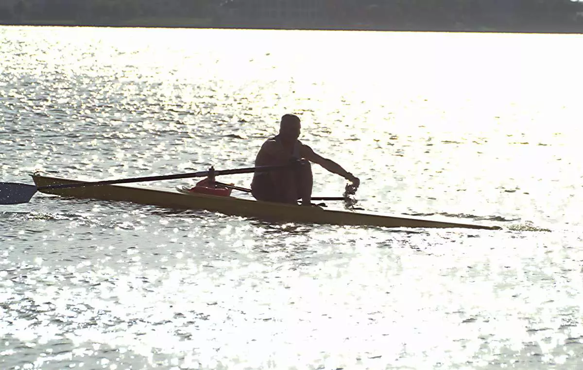 silhouette of man in a racing shell boat rowing from light into dark